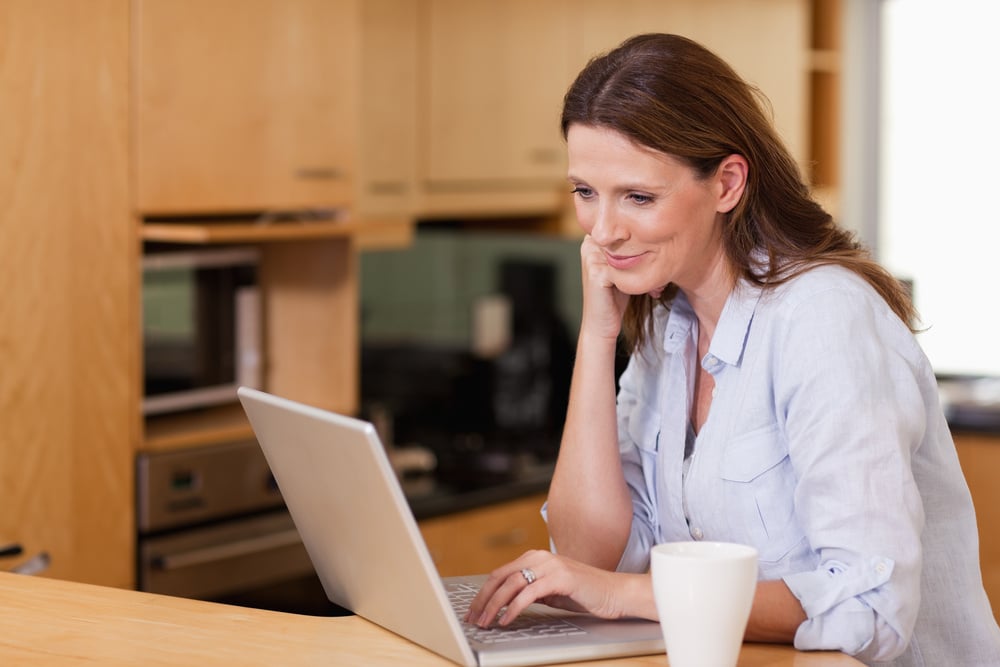 Smiling woman in the kitchen looking at her laptop